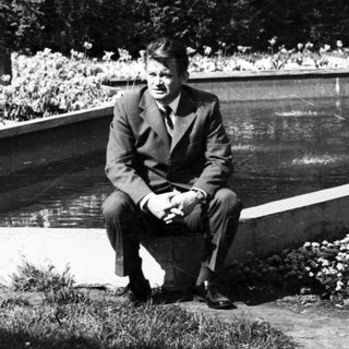 Man sitting by pond in formal attire.