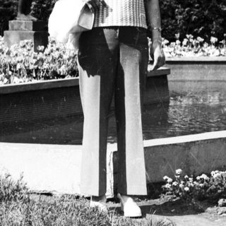 Woman standing in park holding bag near sculpture.