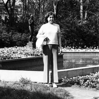 Woman standing in park holding bag near sculpture.