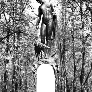 Bronze statue of man with dog in forest setting.