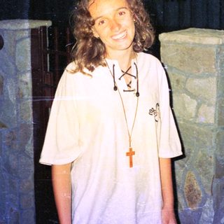 Woman wearing white shirt with religious pendant indoors.