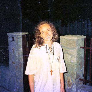Woman wearing white shirt with religious pendant indoors.