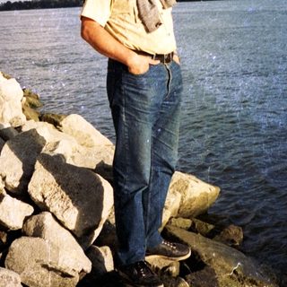 Man standing by rocky riverbank under cloudy sky.