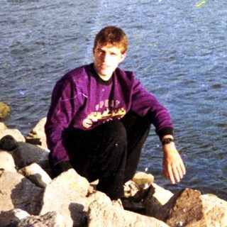 Person fishing near rocky lake shore.