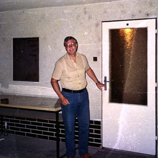 Man standing near open door in aged indoor hallway.