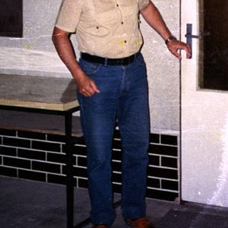 Man standing near open door in aged indoor hallway.