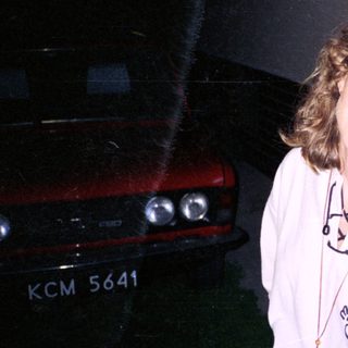Person wearing hoodie with cartoon design, smiling outdoors near car.