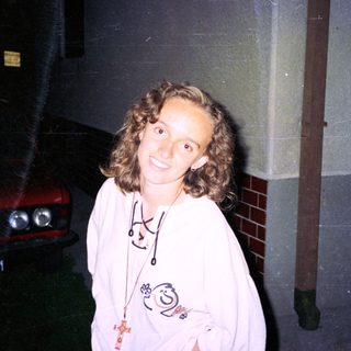 Person wearing hoodie with cartoon design, smiling outdoors near car.