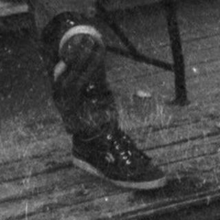 Man sitting on bench outside, holding cup, wearing cap.