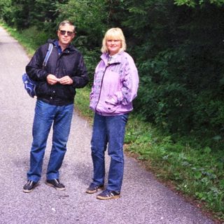 Two people standing on a tree-lined path.