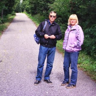 Two people standing on a tree-lined path.