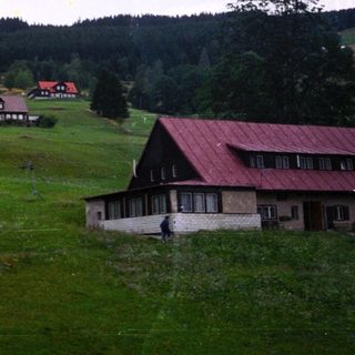 Rural countryside scene with farmhouses and rolling hills.