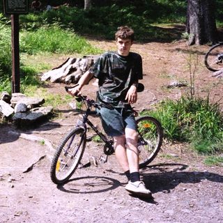 Young man posing with mountain bike near trail map.