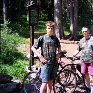 Two men posing with bicycles in a forested area.