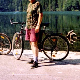 Person standing by lake with two bicycles.