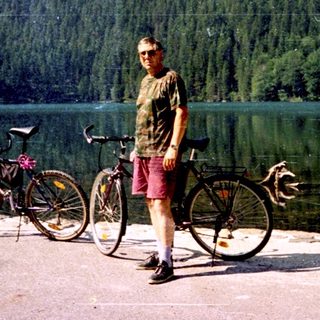 Person standing by lake with two bicycles.