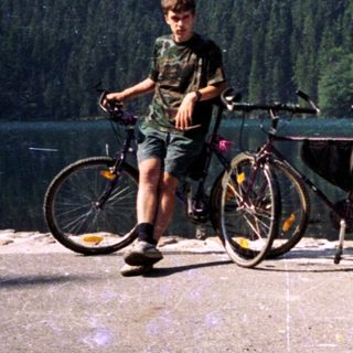 Person standing by lake with two bicycles.