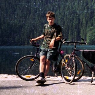 Person standing by lake with two bicycles.