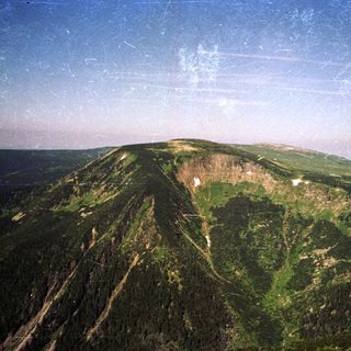 Dense forested mountain peak with rocky summit.