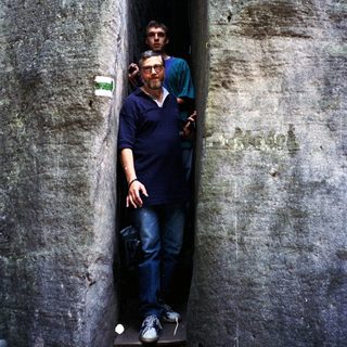 Two men standing in narrow, ancient stone corridor.