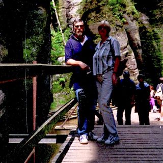 Two people standing on a wooden bridge near rock formations.