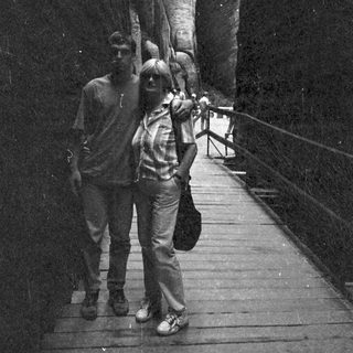 Two people walking on a wooden boardwalk near rock formations.