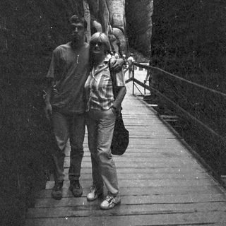 Two people walking on a wooden boardwalk near rock formations.