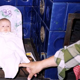 Baby wrapped in towel sitting on stove.