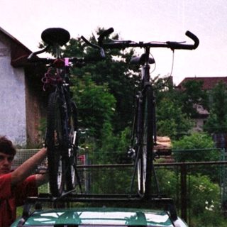Person securing bikes on roof rack of green car.