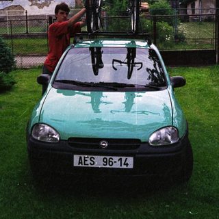 Person securing bikes on roof rack of green car.