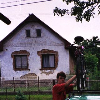 Person securing bikes on roof rack of green car.