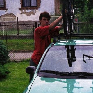 Person securing bikes on roof rack of green car.