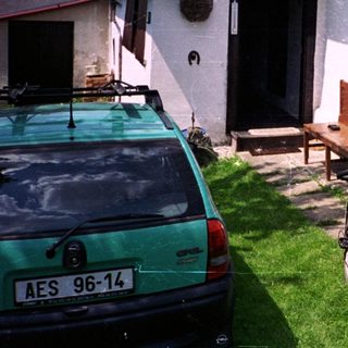 Person in cycling gear stands with bike near house.