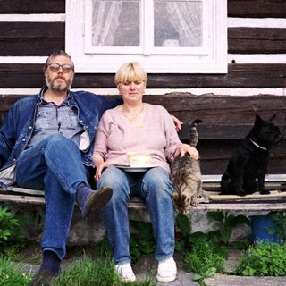 Two people sitting on bench outside rustic wooden house with pets.