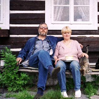 Two people sitting on bench outside rustic wooden house with pets.