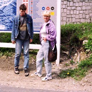 Two people standing near a ski resort advertisement board.