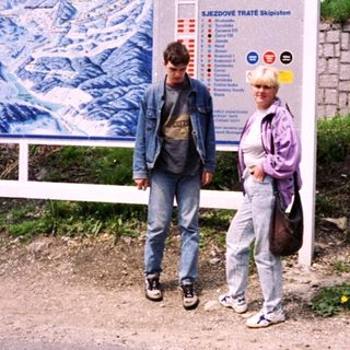 Two people standing near a ski resort advertisement board.