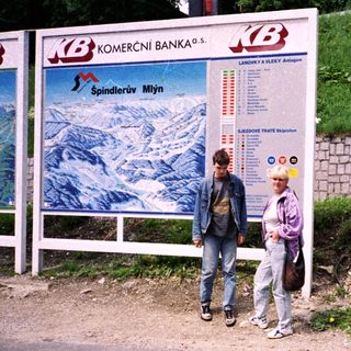 Two people standing near a ski resort advertisement board.