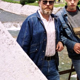 Two men posing by a scenic riverside in a mountainous area.