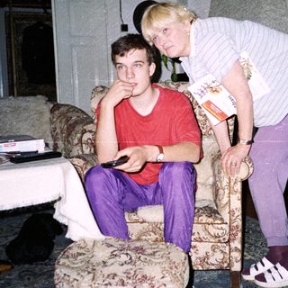 Two people indoors, one leaning on cane.