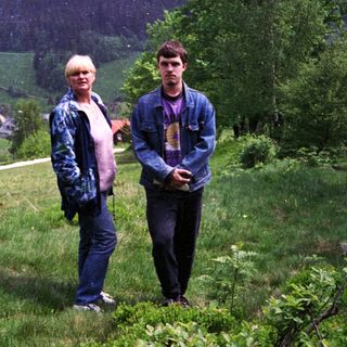 Two people standing outdoors in scenic mountainous countryside.