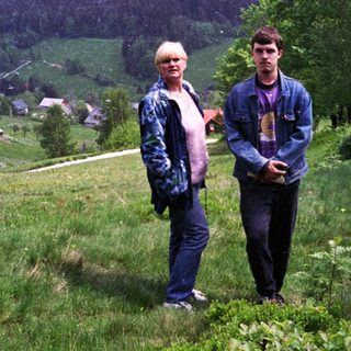 Two people standing outdoors in scenic mountainous countryside.