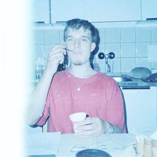 Young man eating while brushing teeth in kitchen.