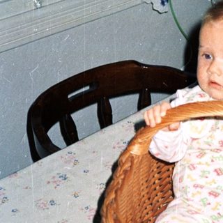 Baby in wicker basket at home table.