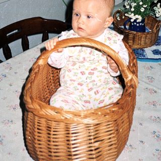 Baby in wicker basket at home table.