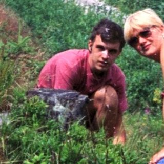 Two people exploring or hiking in a grassy, forested area.