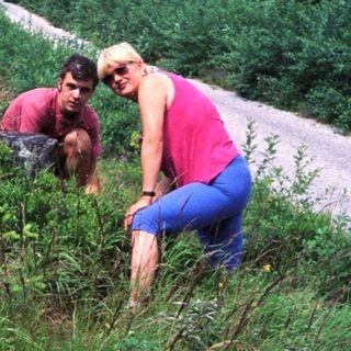 Two people exploring or hiking in a grassy, forested area.