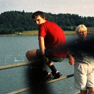 Two people sitting on a railing by a lake.
