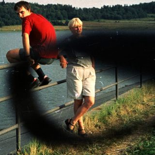 Two people sitting on a railing by a lake.