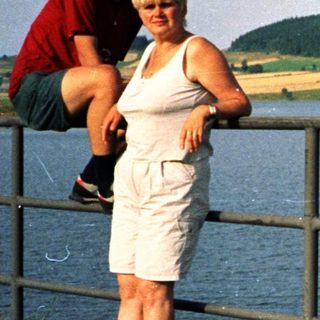 Couple posing by lake with scenic hillside.